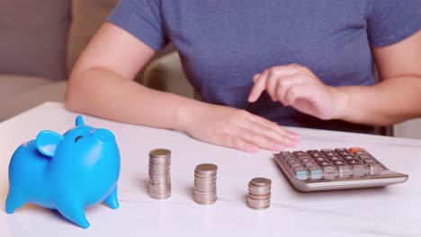 Women-using-calculators-and-putting-coins-in-a-piggy-bank,-saving-money-concept