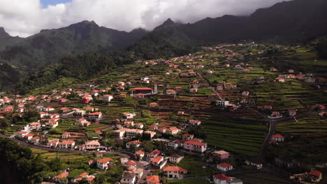 Aerial-view-of-a-small-village-on-top-of-a-green-hill-with-terraced-houses-in-a-mountain-landscape,-Sao-Vicente,-Madeira,-establishing-shot