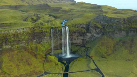 Scenic-view-of-waterfall-cascade-in-green-plateau-landscape,-aerial-push-in-shot-in-Seljalandsfoss-Iceland