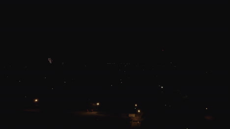 Flying-by-neighborhood-fireworks-in-the-night-sky,-aerial-drone