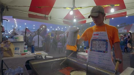 Young-boy-pouring-funnel-cake-batter-into-a-deep-fryer-at-a-festival