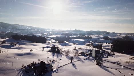 Village-buildings-in-hilly-landscape-covered-in-snow-during-snowfall,-aerial-drone-view