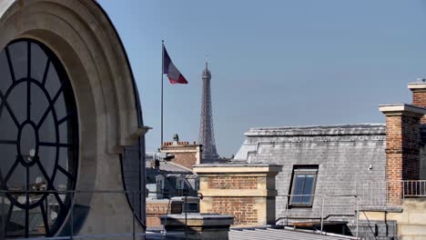 Parisian-round-window-rooftop-With-Eiffel-Tower-and-tricolore-French-Flag-in-the-distance,-Locked-high-shot