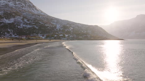 Kleine-Wellen-Laufen-Auf-Den-Arktischen-Sandstrand,-Fleckiger-Schnee-Auf-Den-Bergen