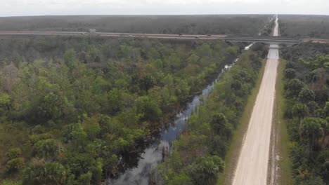 highway-bridge-over-canal-dirt-road-overpass-everglades-expressway-florida-aerial-drone-tilt