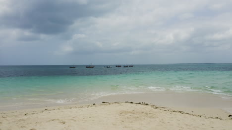 Small-boats-anchored-offshore-white-sand-beach-in-Zanzibar,-drone-shot