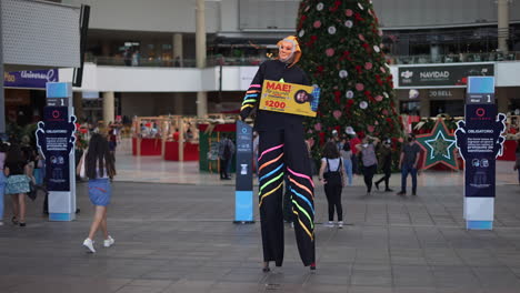 stilt-walker-with-mask,-acrobat-in-costume-in-shopping-mall-next-to-Christmas-tree