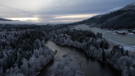 Flyover-moody-icy-landscape-in-Helgeland-Northern-Norway,-foggy-and-stunning-view-towards-the-sun,-above-a-river