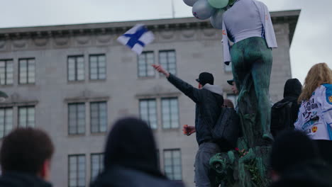 Fan-celebrating-waving-the-Finnish-flag-at-the-Havis-Amanda-statue-in-Helsinki,-Olympic-Ice-hockey-gold-celebrations-in-Finland---slow-motion-shot