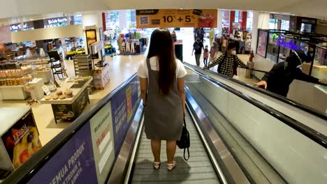 Asian-woman-using-escalator-in-shopping-mall-in-Yogyakarta-Indonesia,-rear-view