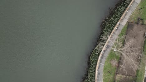 A-top-down-view-of-the-East-River-near-a-park-on-Roosevelt-Island,-NY-on-a-cloudy-day