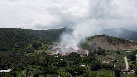 Clouds-of-smoke-billowing-from-rubbish,-trash-and-garbage-being-burned-at-the-landfill-tip-in-rural-green-environment-in-Timor-Leste,-Southeast-Asia,-aerial-drone-view