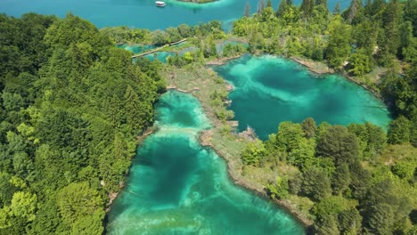 Top-view-of-the-Plitvice-Lakes-National-Park-with-many-green-plants,-beautiful-lakes-and-a-boat-sailing-in-these-lakes