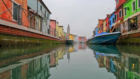 Unusual-water-surface-pov-view-of-Burano-colorful-houses-and-canal-with-moored-boats,-Italy
