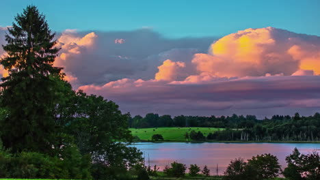 Dense-clouds-lighting-by-golden-sunset-flying-over-natural-lake-in-rural-area,time-lapse