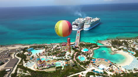 Wide-rotating-drone-shot-of-CoCoCay-island-with-water-slides-and-a-Royal-Caribbean-cruise-ship-in-the-background,-with-hot-air-ballon