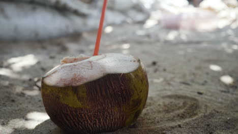 Fresh-natural-coconut-coco-water-drink-on-the-sandy-beach-with-plastic-straw-in-Puerto-Escondido,-Mexico
