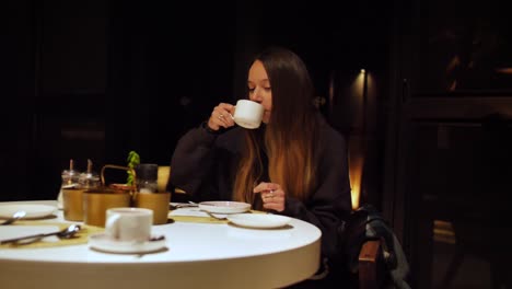 Slow-motion-shot-of-a-young-woman-sitting-in-the-dark-at-the-breakfast-table-drinking-her-coffee
