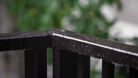 Eckgeländer-Auf-Einem-Balkon-Mit-Strömendem-Regen,-Der-Auf-Die-Oberfläche-Spritzt,-Mit-Einem-Verschwommenen-Gartenhintergrund