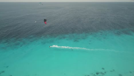 Drohnenaufnahme-Eines-Kitesurfers,-Der-Mit-Hoher-Geschwindigkeit-Auf-Einem-Wunderschönen-Türkisfarbenen-Meer-Fährt