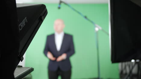 Television-presenter-talking-to-camera-using-a-teleprompter-in-a-green-screen-studio