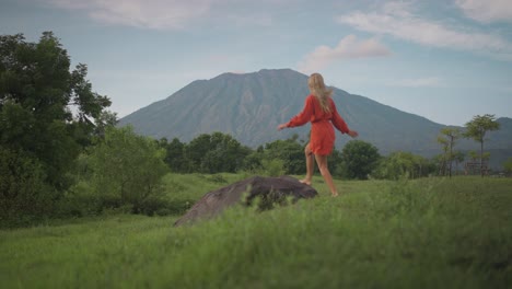 Mujer-Despreocupada-Corriendo-Hacia-La-Roca-Y-Disfrutando-De-Una-Vista-Impresionante-Del-Monte-Agung,-Savana-Tianyar