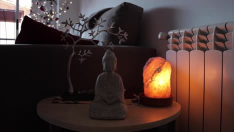 small-statue-of-Buddha-sitting-in-the-shape-of-a-lotus-flower-next-to-a-nale-himalaya-natural-satl-lamp-stone-and-a-small-metal-tree-behind-in-the-living-room