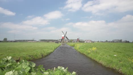 Landschaft-Mit-Traditionellen-Windmühlen-An-Einem-Teich-Auf-Einer-Grünen-Wiese---Totalaufnahme