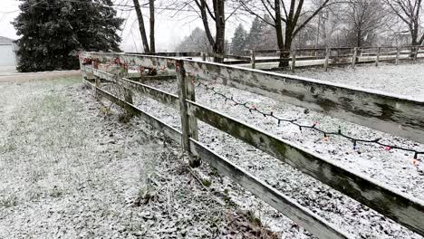 Wooden-farm-fence-decorated-with-Christmas-lights-during-heavy-snowfall