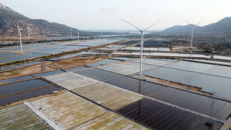 Vista-Aérea-De-La-Granja-De-Estanques-Salinos-Con-Molino-De-Viento-Turbina-Eólica-Suministro-De-Energía-Verde-Agricultura-Sostenible-En-Vietnam-Asia