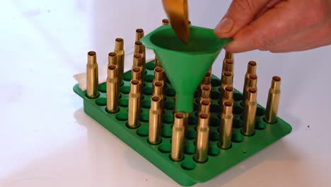 Person-filling-empty-brass-casing-with-gunpowder-through-funnel-during-home-reloading-process---Static-closeup-of-hand-and-tray-with-caliber-3006-empty-brass-casings
