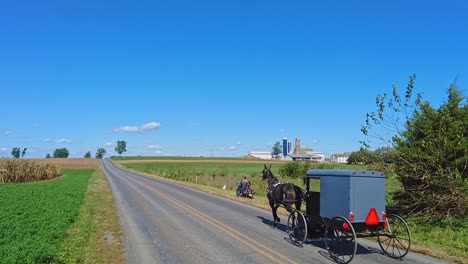 An-Amish-Horse-and-Buggy-Trotting-Down-a-Country-Road-Passing-Farms,-in-Slow-Motion-on-a-Beautiful-Sunny-Day