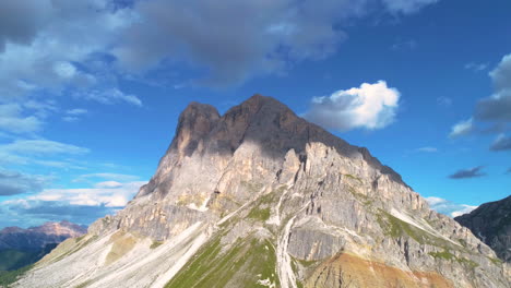 Aerial-view-orbiting-steep-Peitlerkofel-South-Tyrol-Dolomites-rocky-mountain-summit-against-blue-cloudy-sky
