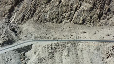 aerial-drone-tracking-a-local-white-car-on-the-dirt-highway-road-in-the-rugged-mountains-of-Skardu-Pakistan-along-the-Indus-River-Valley-on-a-sunny-summer-day