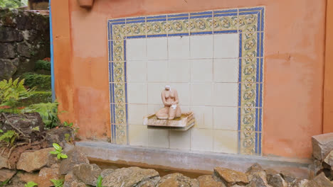 Tracking-view-of-small-tile-fountain-with-female-sculpture-and-rock-walls-with-plants