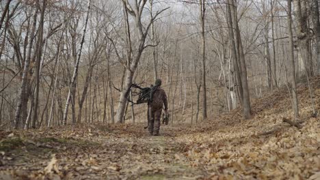 Bowhunter-in-camouflage-clothing-carrying-hunting-equipment,-walking-alone-in-forest