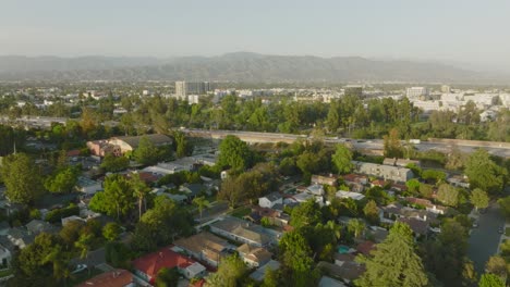 Flying-Over-North-Hollywood-in-San-Fernando-Valley,-Busy-Freeway-with-Mountains-on-Horizon
