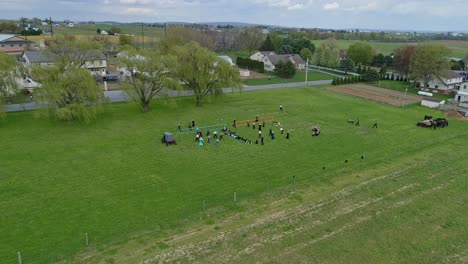Eine-Drohnenansicht-Von-Amish-Farmland-Und-Gehöften-Und-Sich-Nähernden-Amish-Teenagern,-Die-An-Einem-Sonnigen-Tag-Volleyball-Spielen