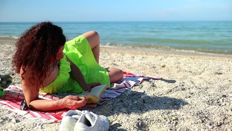 red-haired-caucasian-girl-in-green-dress-relaxes-in-the-sun-at-the-beach-reading-a-book-with-the-breeze-moving-her-red-hair,-static-shot