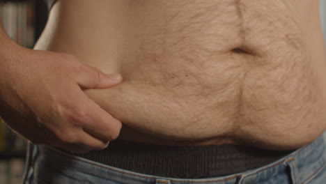 Close-up-of-hand-grabbing-love-handle-of-fat-shirtless-man