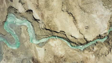 Dead-Sea-Hot-Springs-dramatic-wide-aerial-top-down-shot-following-desert-canyon-landscape-with-crystal-clear-warm-waters-and-rock-pools