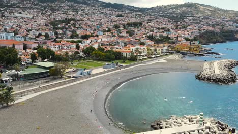 Aerial-pan-shot-of-Funchal-coastal-town-in-Madeira-island,-Portugal-surrounded-by-a-mountain-range-at-daytime
