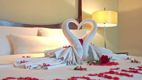 Pan-of-linen-sculpture-of-swans-forming-a-heart-on-a-bed-covered-with-red-roses-and-red-rose-petals