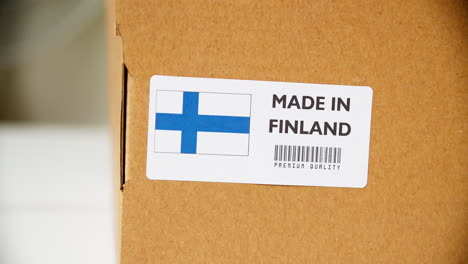 Hands-applying-MADE-IN-FINLAND-flag-label-on-a-shipping-cardboard-box-with-products