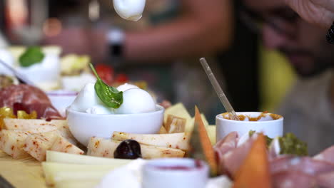 Restaurant-Gastronomy-Dinner-Buffet-and-Aperitif,-Hors-D'oeuvre-and-Assortment-of-Various-Appetizers,-Mozzarella-Cheese-Prosciutto,-Blurred-Background-Woman's-Hand-Takes-Piece-of-Mozzarella-with-Fork