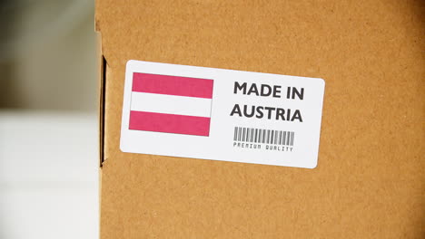 Manos-Aplicando-La-Etiqueta-De-La-Bandera-De-Austria-Hecha-En-Una-Caja-De-Cartón-De-Envío-Con-Productos