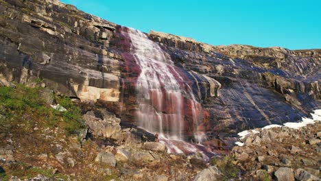 Aerial-View-Of-Waterfall-Cascading-Down-Red-Coloured-Rock-Face-At-Hardangervidda-National-Park