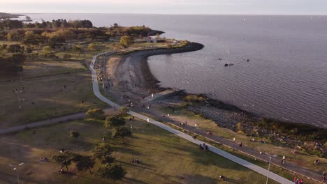 Aerial-view-of-Vicente-Lopez-coastal-park-with-many-people-and-tranquil-water-of-Atlantic-Ocean-at-sunset---Panorama-wide-shot