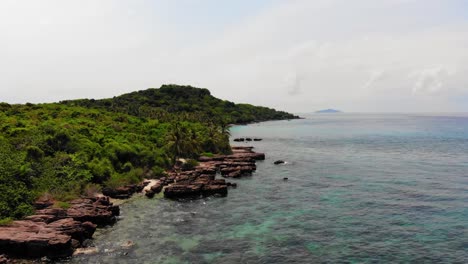 Flying-Low-over-Rocky-Coast,-Clear-Turquoise-Waters-and-Brightly-Colored-Coral-Reefs,-Wild-Tropical-island-in-Phu-Quoc-Region,-Vietnam-Archipel