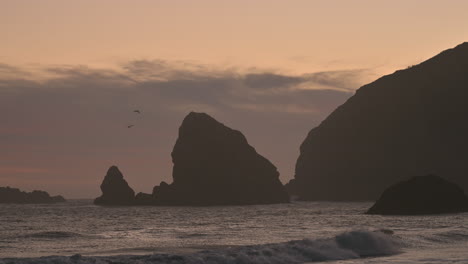 Oregon-Küstensonnenuntergang-Mit-Silhouettierten-Felsen-Und-Fliegenden-Vögeln
